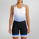 A woman modeling a sleeveless athletic one-piece unisuit with a white upper section, blue and white horizontal stripes across the midsection, and black lower shorts with blue and white trim, set against a plain light gray studio background.