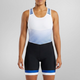 A woman modeling a sleeveless athletic one-piece unisuit with a white upper section, blue and white horizontal stripes across the midsection, and black lower shorts with blue and white trim, set against a plain light gray studio background.