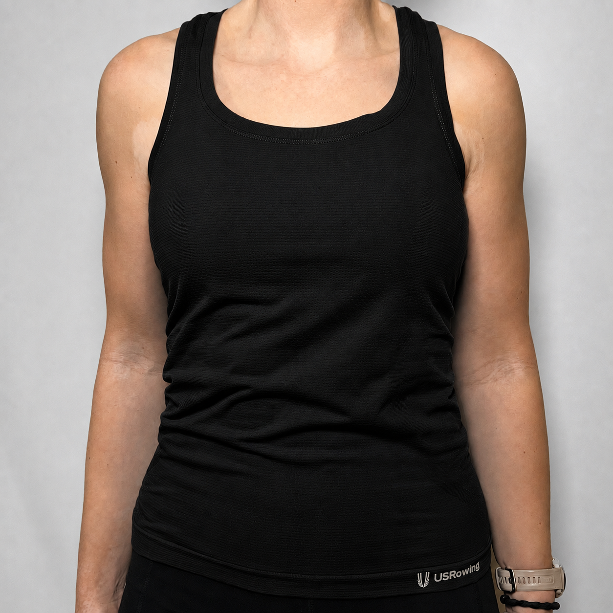 A black knitted tank top worn by a model, featuring a scoop neck and a small white USRowing logo near the bottom hem, set against a plain gray background.