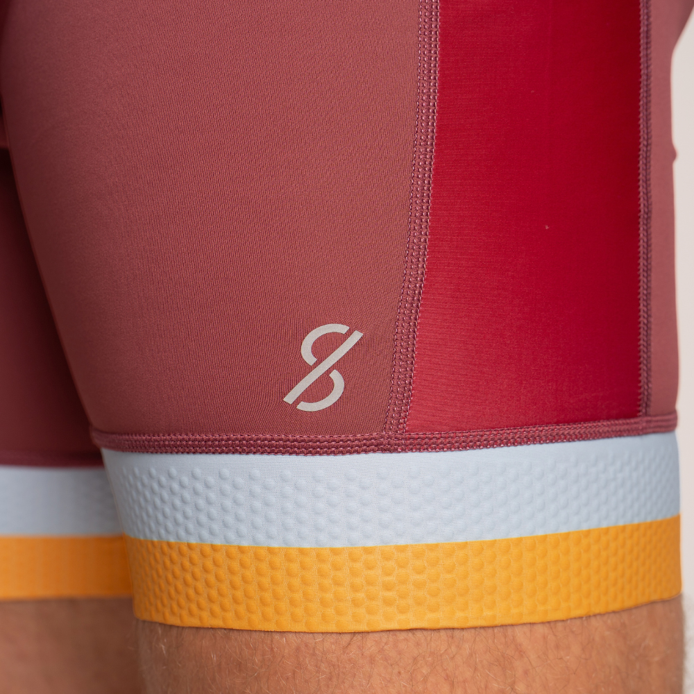 Close-up of the bottom of a unisuit that is a muted brick red color, featuring a white textured band and a yellow grip-tape style band at the bottom, with a small white Strokeside logo on the side.