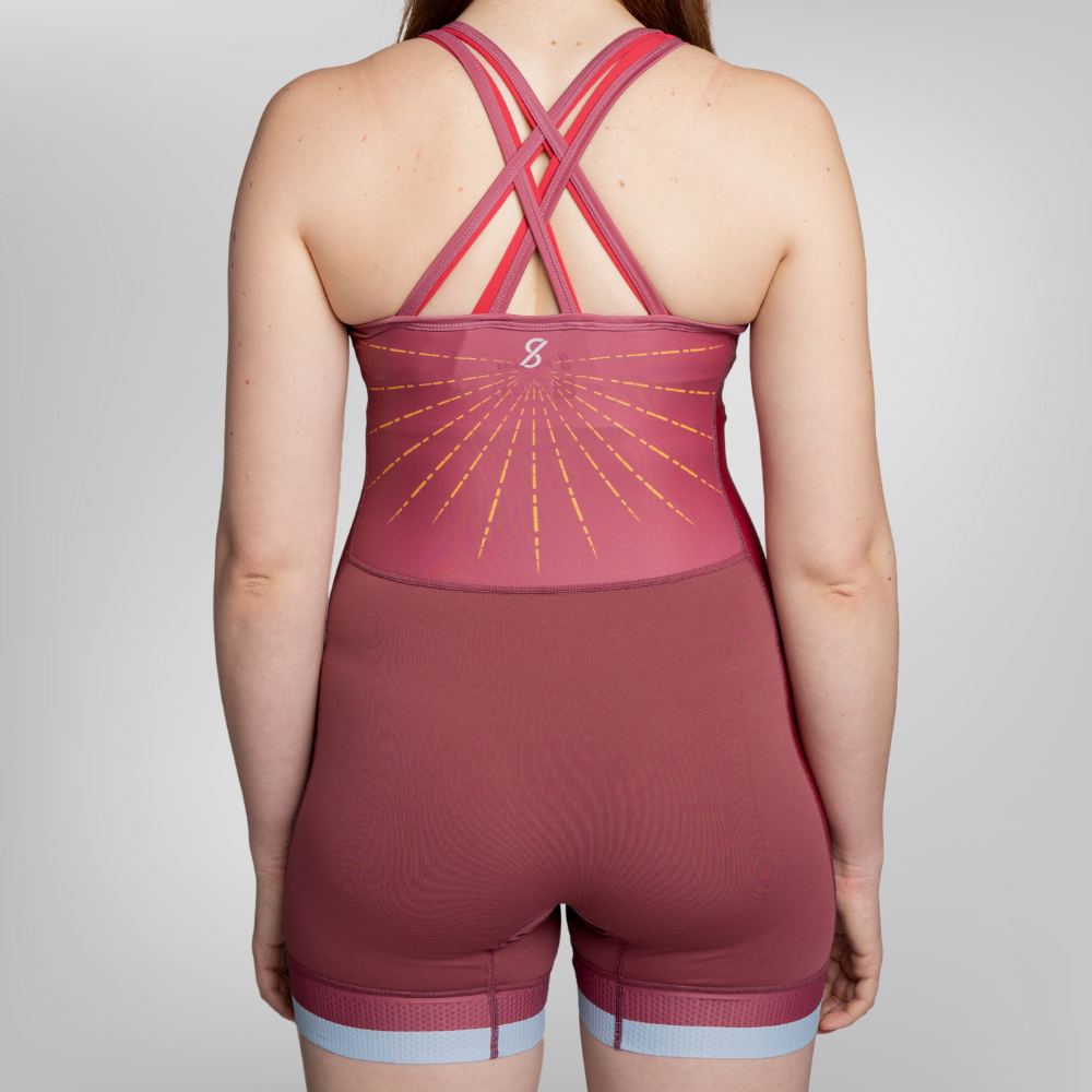 Rear view of a model wearing a maroon uni with crisscross back straps, a sunburst graphic.