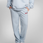 A person wearing a light blue sweatshirt and matching sweatpants with a small red embroidered USRowing logo on the left hip, shown against a plain light gray studio background.