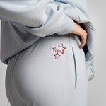 Close-up of a person wearing light blue sweatpants with a red embroidered star design on the back pocket, paired with a matching light blue sweatshirt.