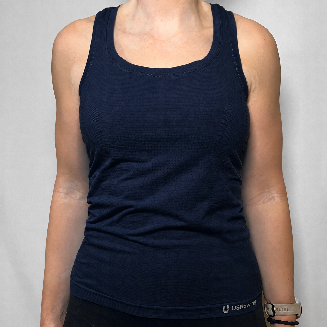 A woman wearing a dark navy blue knitted tank top with a scoop neck, shown from the shoulders to the waist against a light gray background.