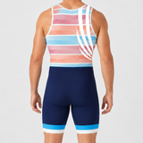 A man viewed from the back wearing a rowing unisuit with a striped pattern in pink, orange, light blue, and white, paired with white socks and shoes, against a light gray studio background.